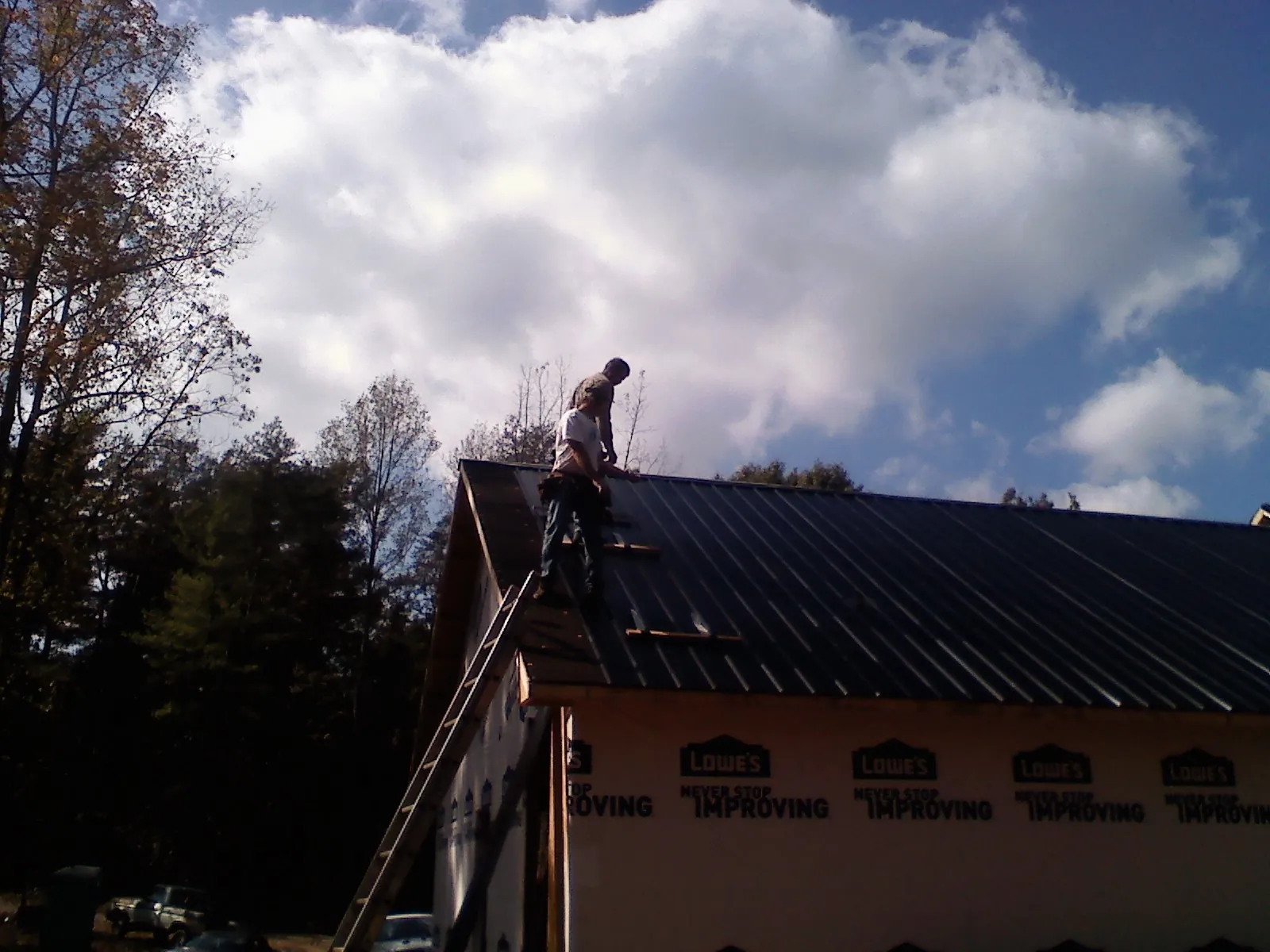 Roofer fastening dark metal panels high against a cloudy sky, from a Roof Inspection job in Harrah
