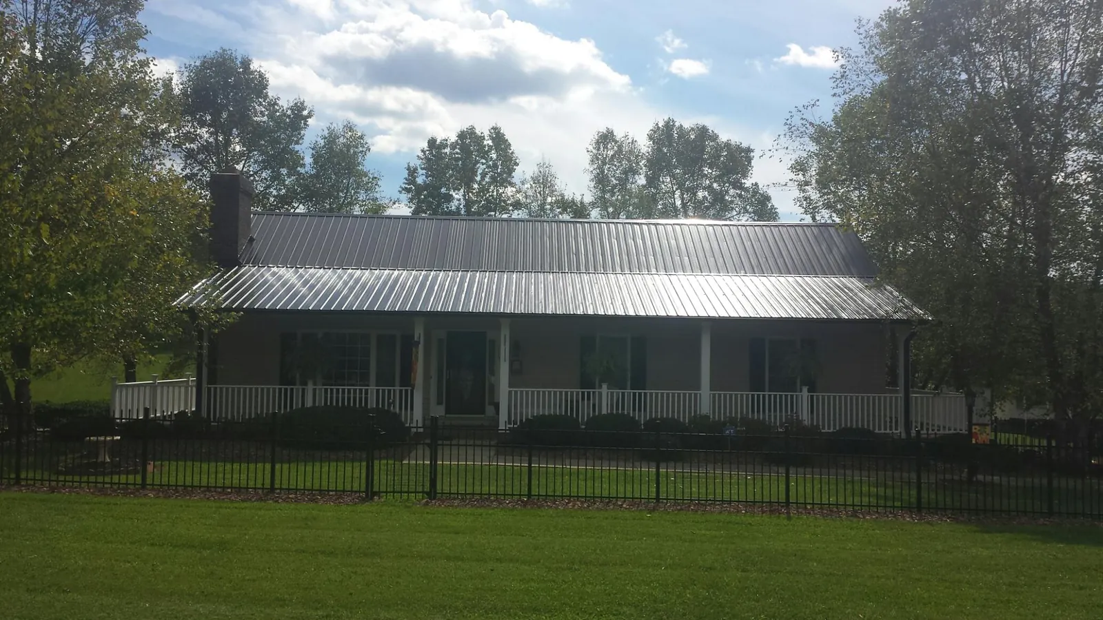 Gray metal roof on a brick ranch with a full width front porch — Gutter Guard Installation work by our crew in Harrah