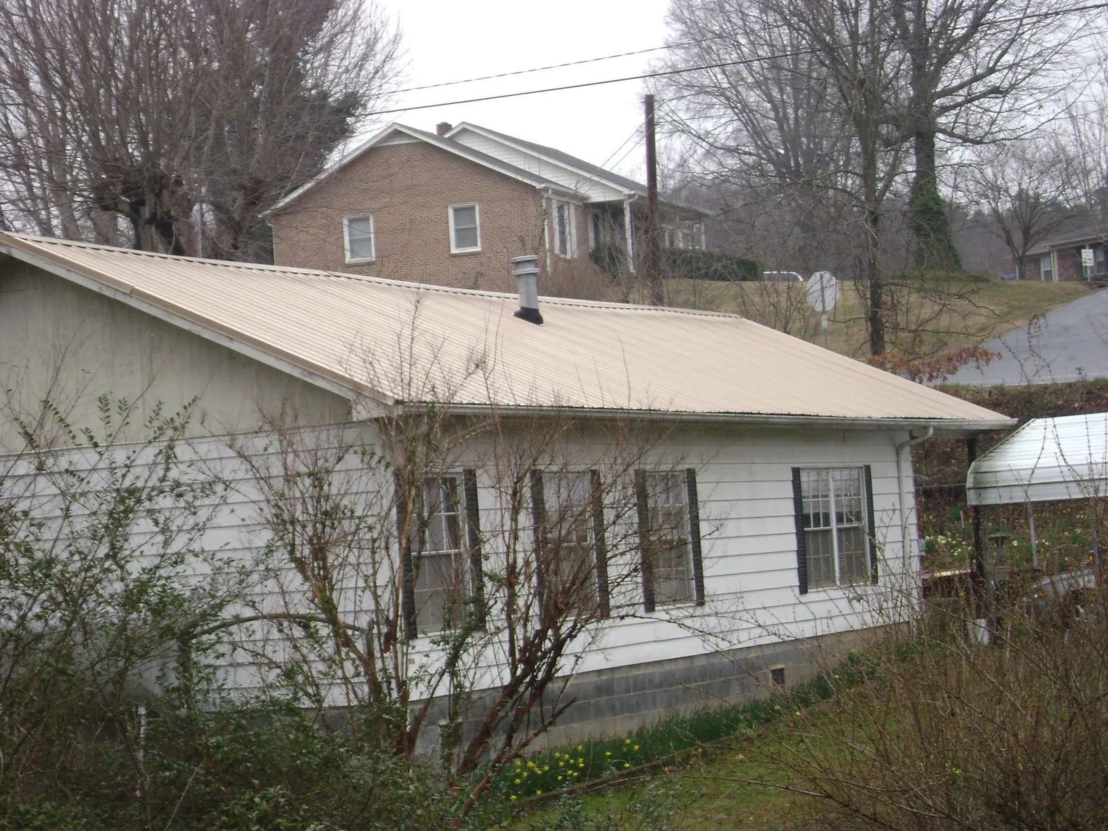 Tan metal roof on a white sided house set into a hillside — Commercial Roofing by Roofing Brothers in Harrah